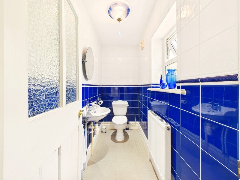 Modern bathroom with blue tile walls, white sink, toilet, and shower enclosure
