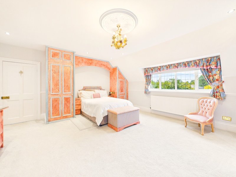 Bright bedroom with ornate orange wardrobe, single bed, pink chair and large window