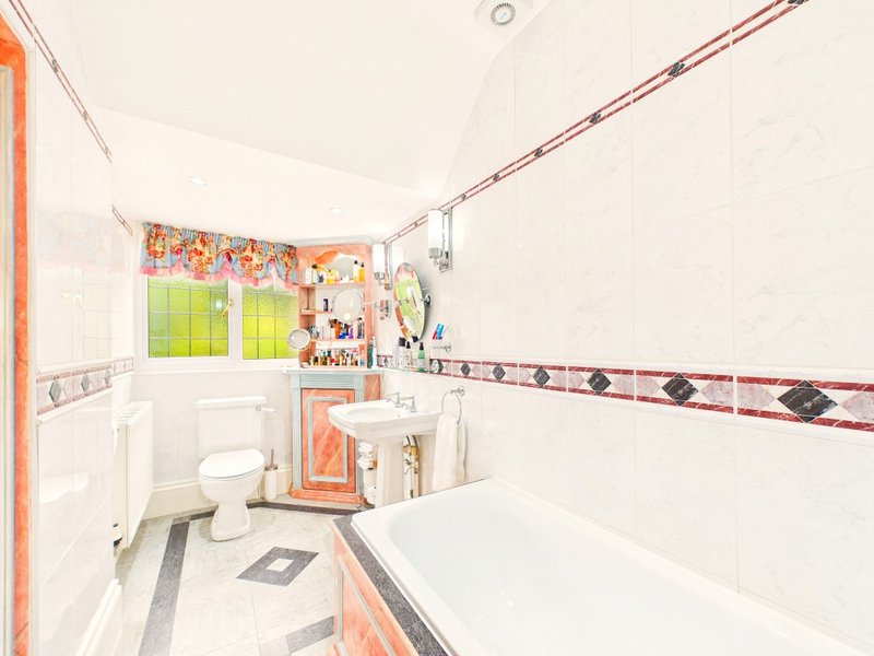 Bright bathroom with white tiles, bathtub, toilet, sink and small window with green outdoor view