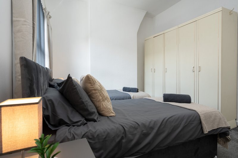 Bedroom with double bed, dark bedding, decorative pillows, wardrobe and bedside lamp
