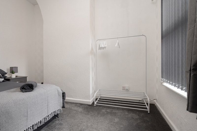 Compact bedroom with single bed, metal clothes rail and vertical blinds on window