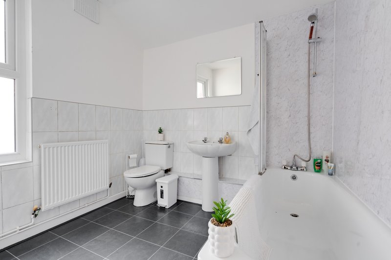 Bright modern bathroom with white suite, dark tile floor, mirror and window