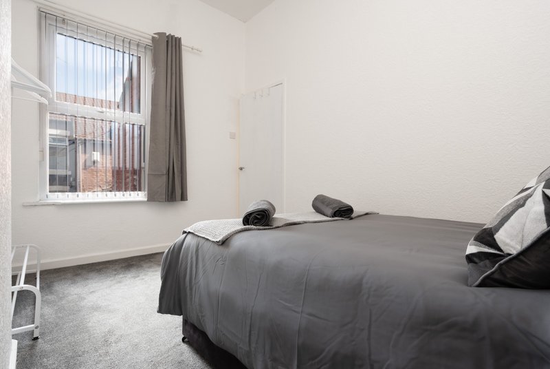 Modest bedroom with double bed, grey bedding, window with curtains and radiator