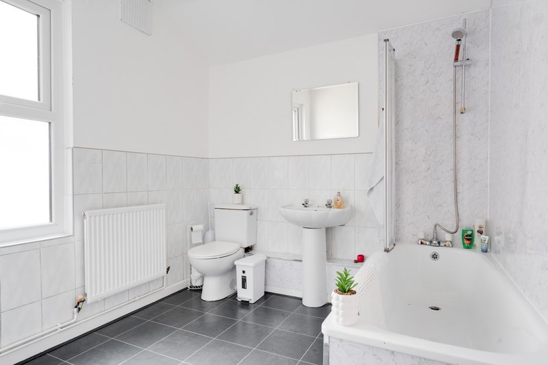 Modern bathroom with white tiles, toilet, sink, shower bath and dark floor