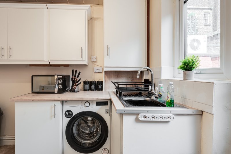Modern kitchen with white cabinetry, integrated washing machine, gas hob, and window with plant