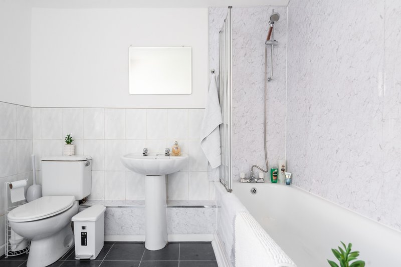 Clean modern bathroom with toilet, pedestal sink, bathtub, shower and tiled walls