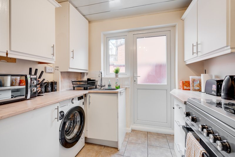 Modern kitchen with white units, washing machine, electric oven and door to garden
