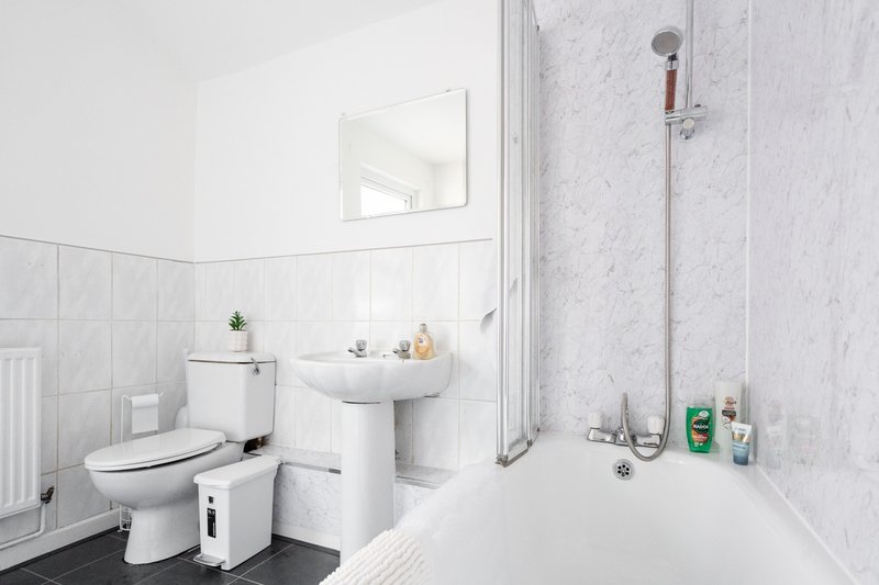 Clean modern bathroom with white toilet, pedestal sink, mirror, and shower enclosure