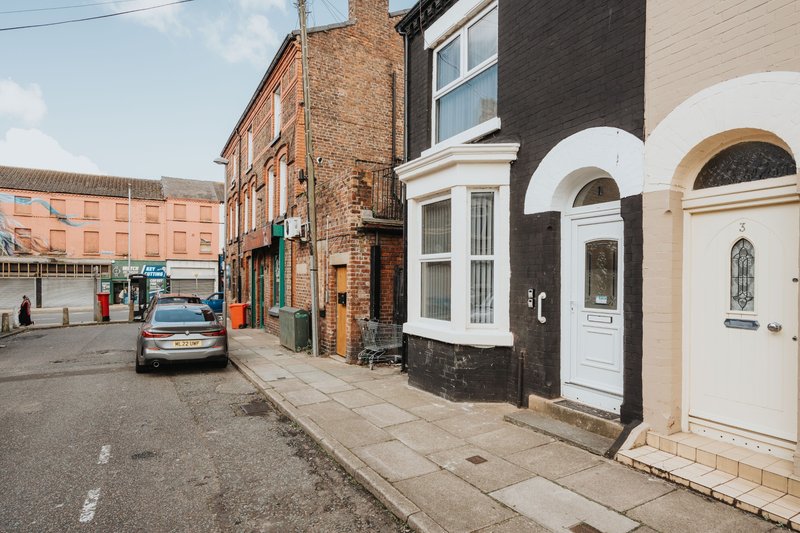 Street view of Victorian brick townhouses with white doors and windows, parked car visible