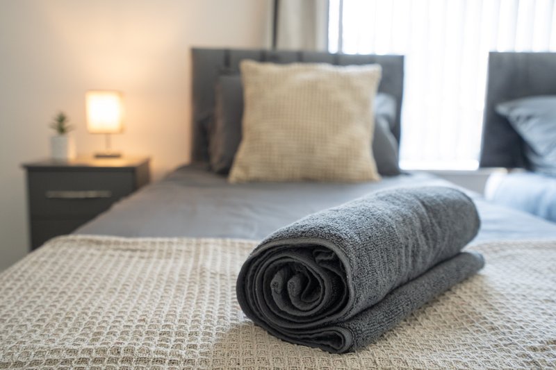 Modern bedroom with rolled grey towel on bed, bedside lamp and dark headboard