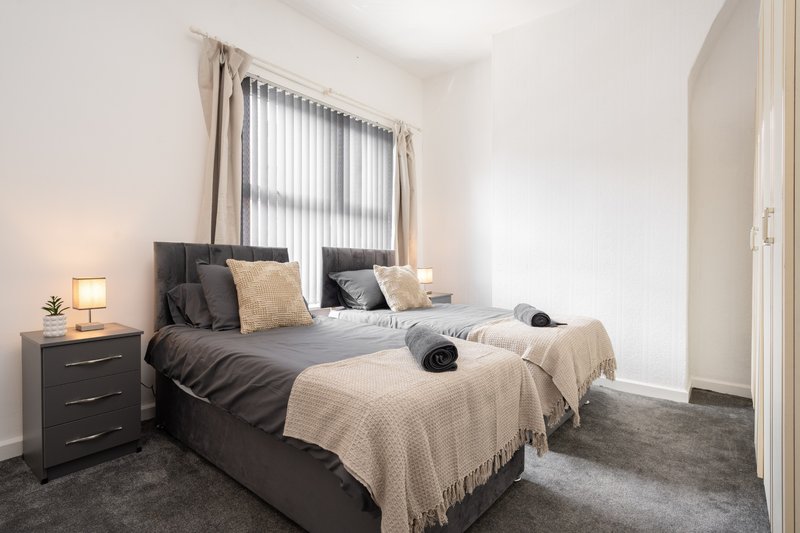 Modern bedroom with two single beds, dark bedding, cream throws, and bedside lamp