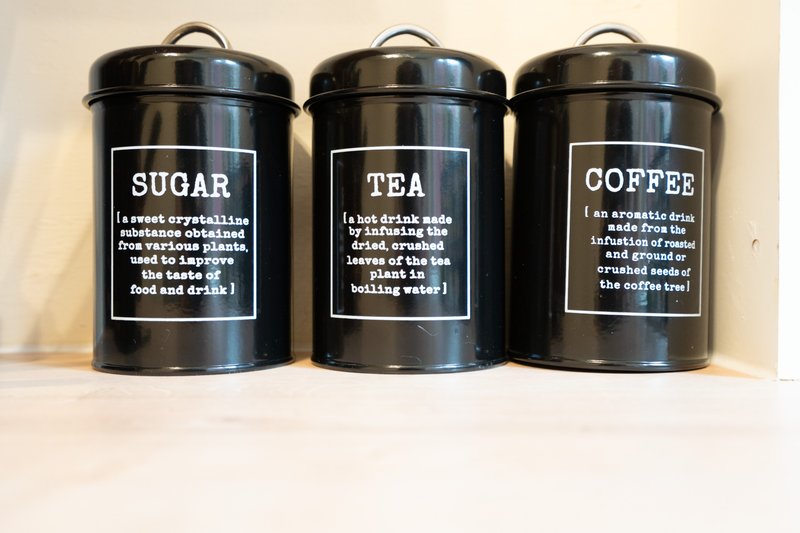 Three black metal storage canisters labeled sugar, tea, and coffee on a shelf