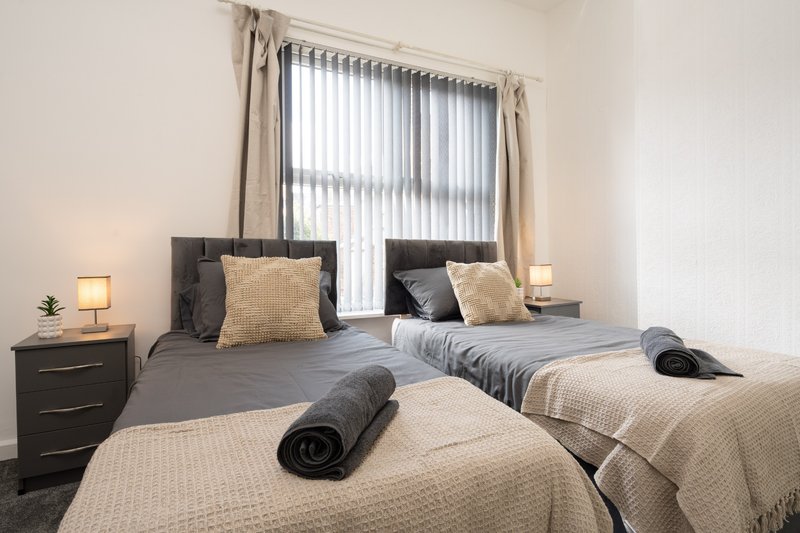 Modern bedroom with two single beds, dark headboard, bedside tables, and vertical blinds on window