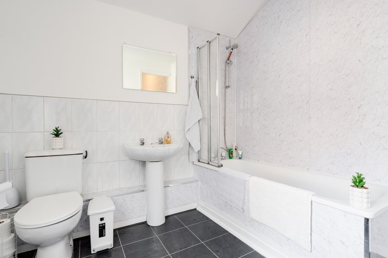 Modern bathroom with white subway tiles, pedestal sink, toilet, bathtub and dark tile flooring