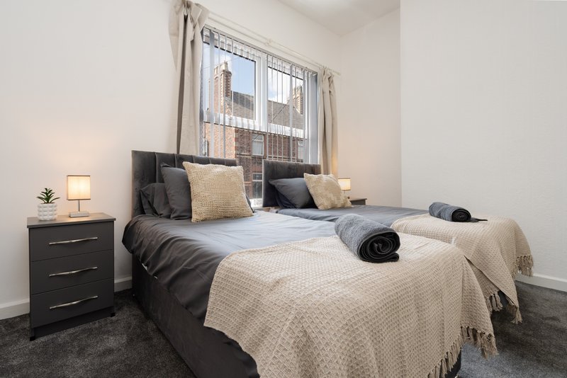 Modern bedroom with double bed, black nightstand, lamp, and city view through window