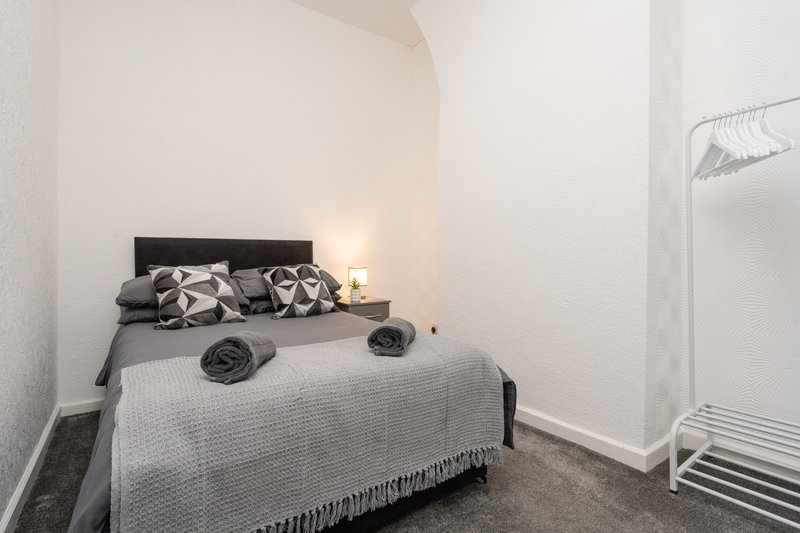 Small bedroom with double bed, black headboard, patterned pillows and white radiator