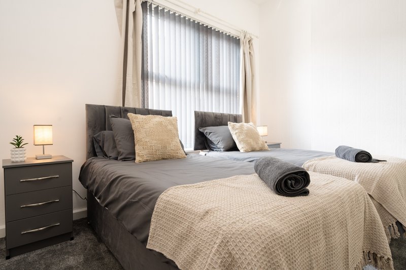 Modern bedroom with two beds, dark bedding, cream throw blankets, and bedside lamp
