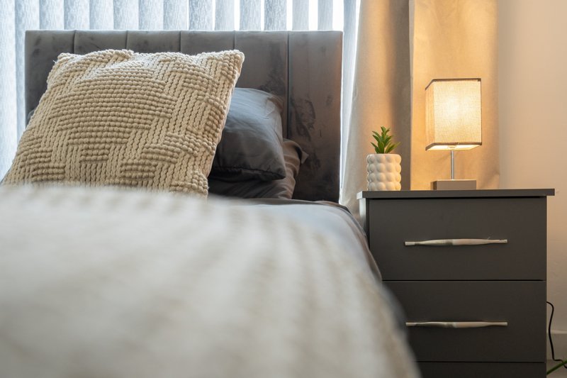 Modern bedroom with grey upholstered headboard, white bedding, textured pillows and black nightstand