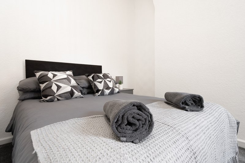 Modern bedroom with black headboard, grey bedding, patterned pillows and rolled towels