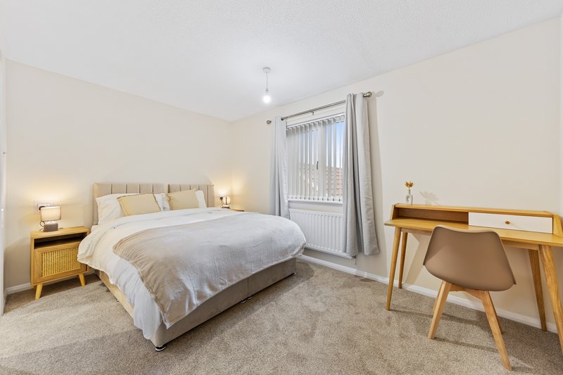 Bright modern bedroom with double bed, wooden furniture, desk, and balcony door