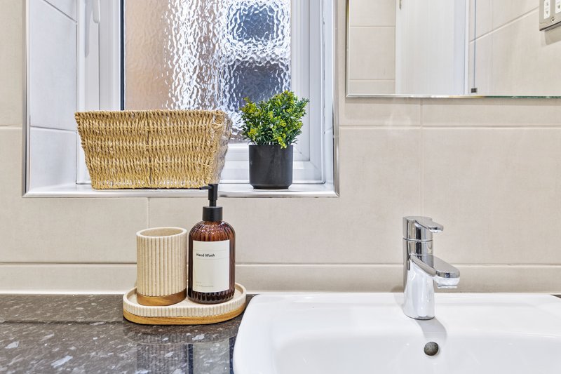 Modern bathroom sink with styled countertop, window with plant and basket, minimalist décor