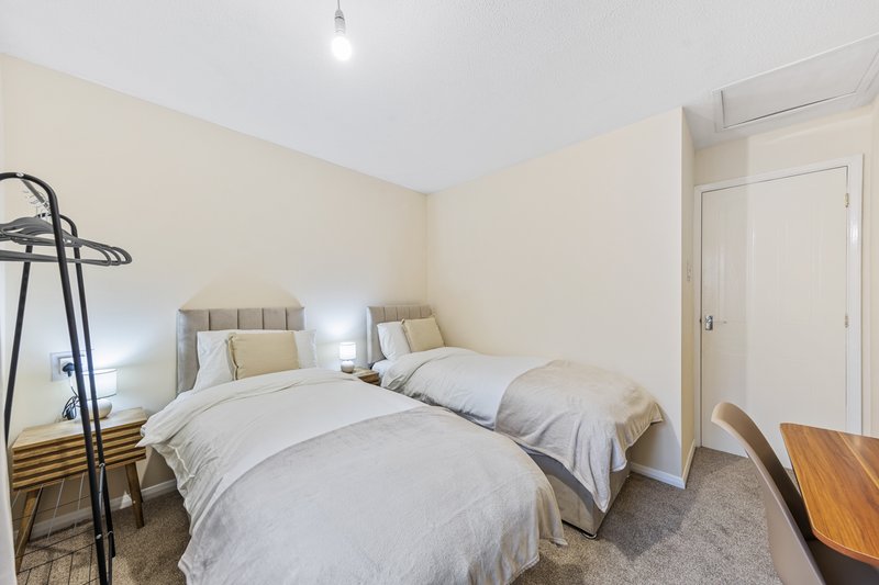 Bright bedroom with two single beds, neutral bedding, cream walls, and wooden desk