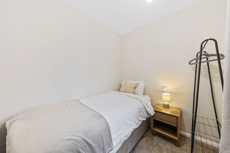 Bedroom with single bed, wooden bedside table, lamp, and coat stand