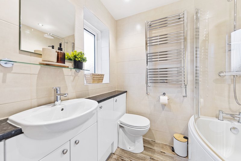 Modern bathroom with curved white sink, toilet, heated towel rail and shower enclosure