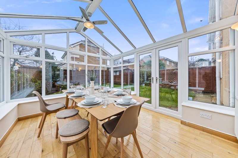 Bright conservatory with wooden dining table, modern chairs, and glass roof overlooking garden