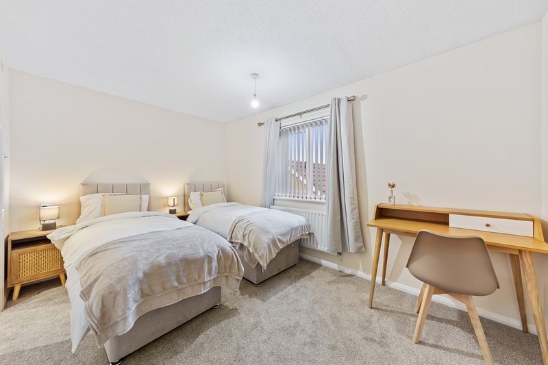 Twin bedroom with two beds, wooden desk, chair and bedside lamps