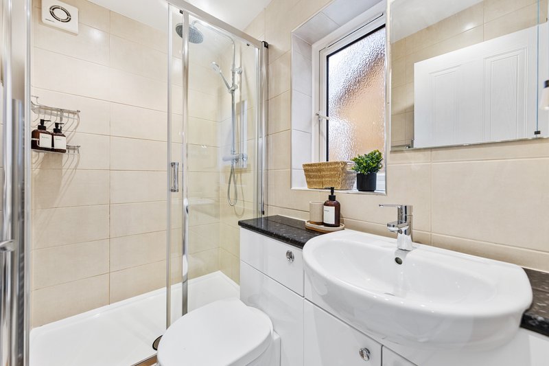 Modern bathroom with white sink, toilet, shower enclosure and beige tiling
