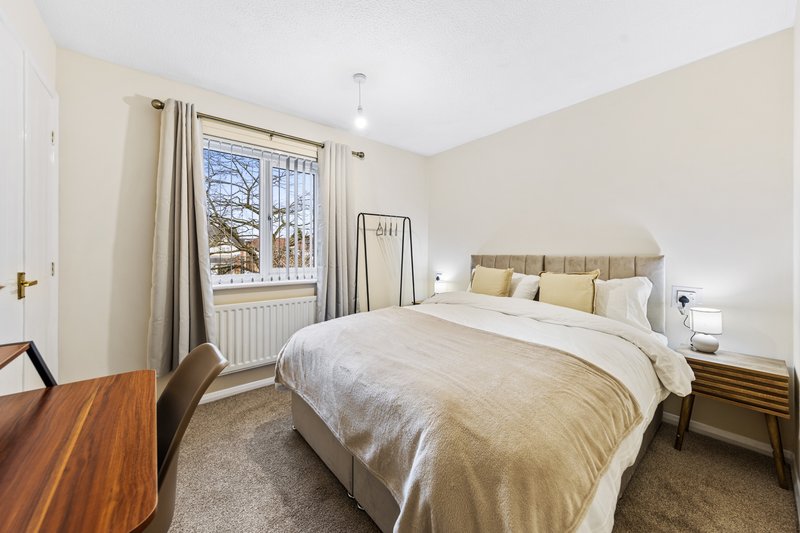 Bright bedroom with double bed, wooden desk, window with curtains and radiator