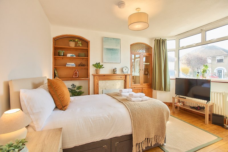 Bright bedroom with double bed, wooden furniture, shelving, TV, and large windows with countryside view