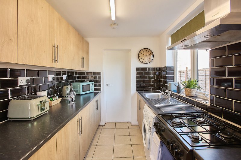Modern galley kitchen with wooden cabinets, black subway tile backsplash, gas cooker and stainless steel appliances