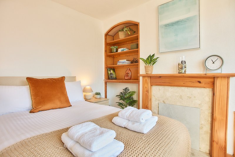 Bedroom with double bed, wooden fireplace surround, shelving unit, and folded towels on bed