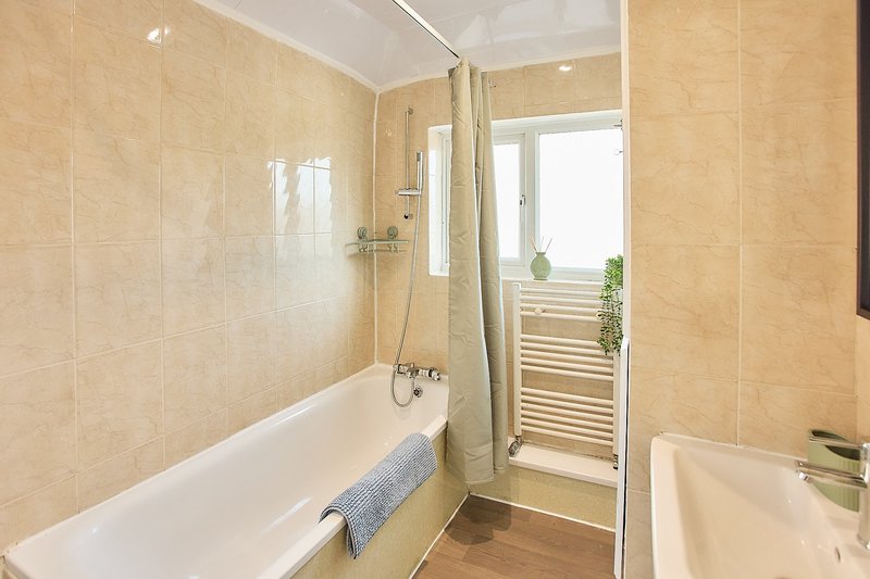 Bathroom with bathtub, shower enclosure, beige tiles, and heated towel rail