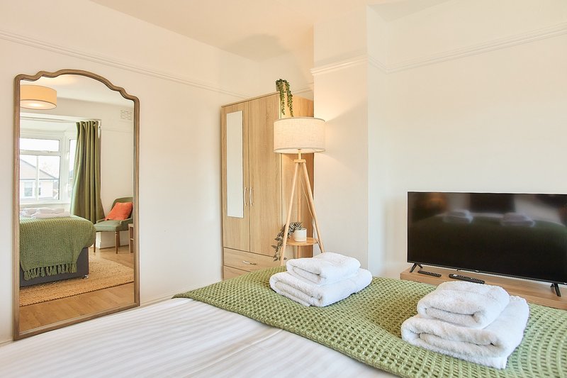 Bright bedroom with two beds, wooden mirror, tripod lamp, TV, and green bedding