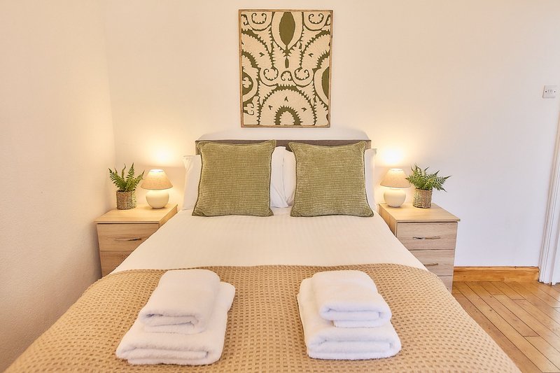 Bedroom with double bed, neutral bedding, bedside tables with lamps and plants, wooden floor