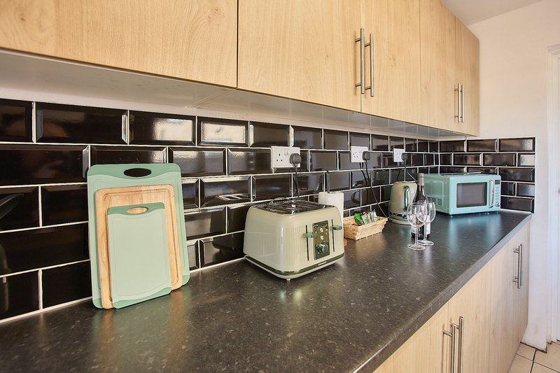 Modern kitchen with light wood cabinets, black tile backsplash, dark countertop and small appliances