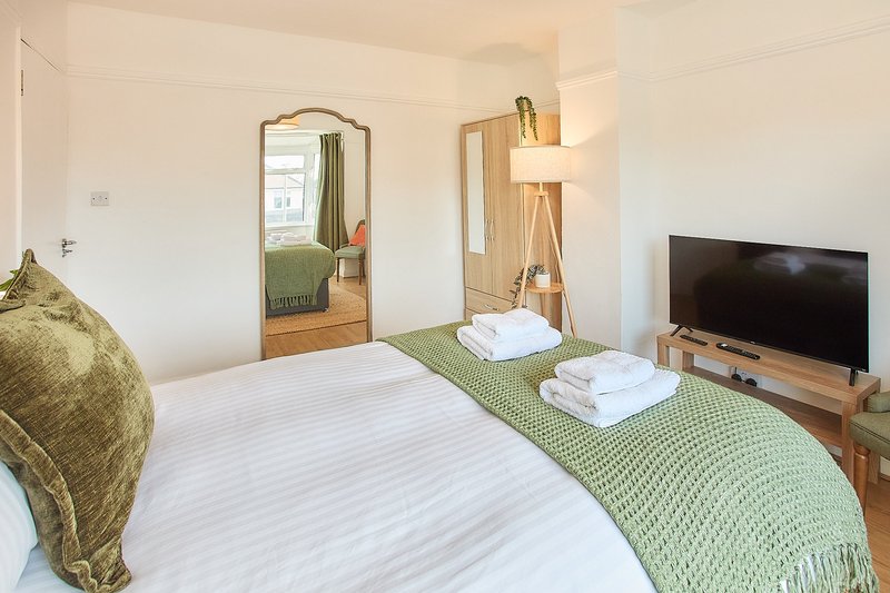 Modern bedroom with double bed, green bedding, wooden furniture, mirror and television