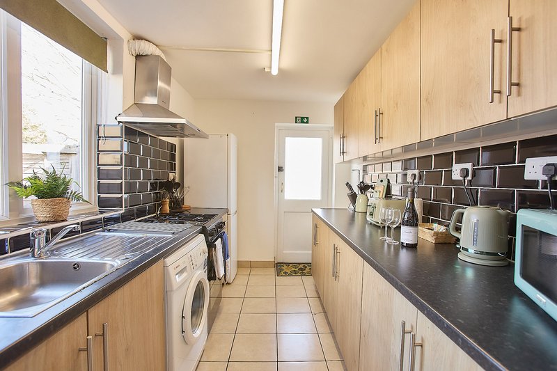 Galley kitchen with light wood cabinets, black countertops, stainless steel appliances and tile backsplash