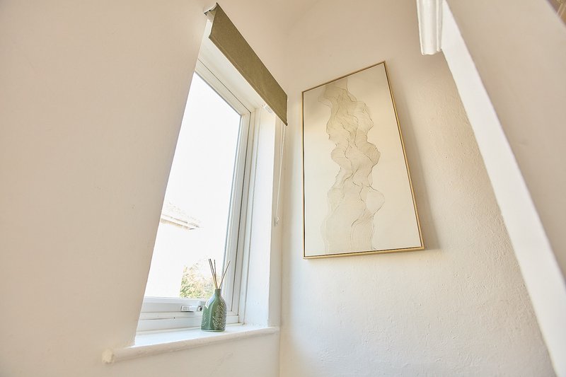 Bright stairwell with window, potted plant on sill, and framed botanical print on wall