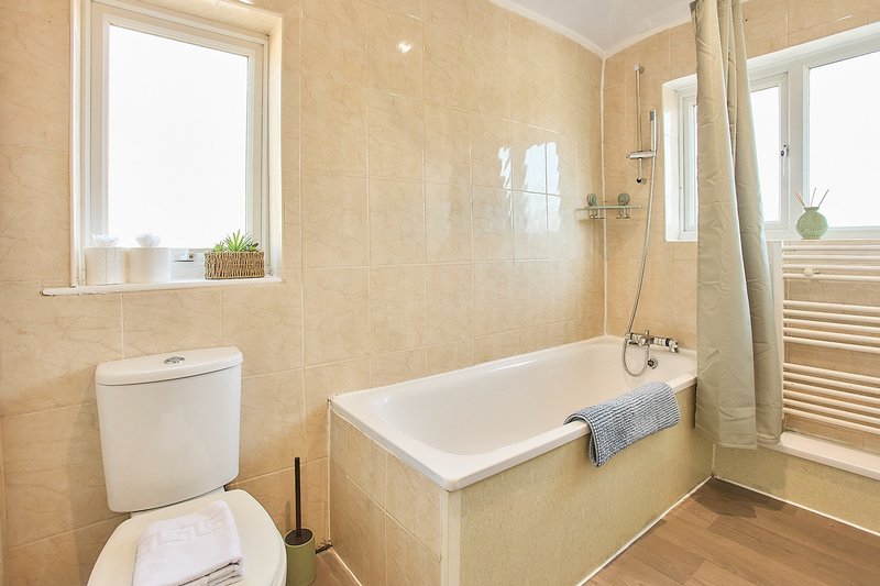 Beige-tiled bathroom with white toilet, bathtub, shower enclosure, window and heated towel rail