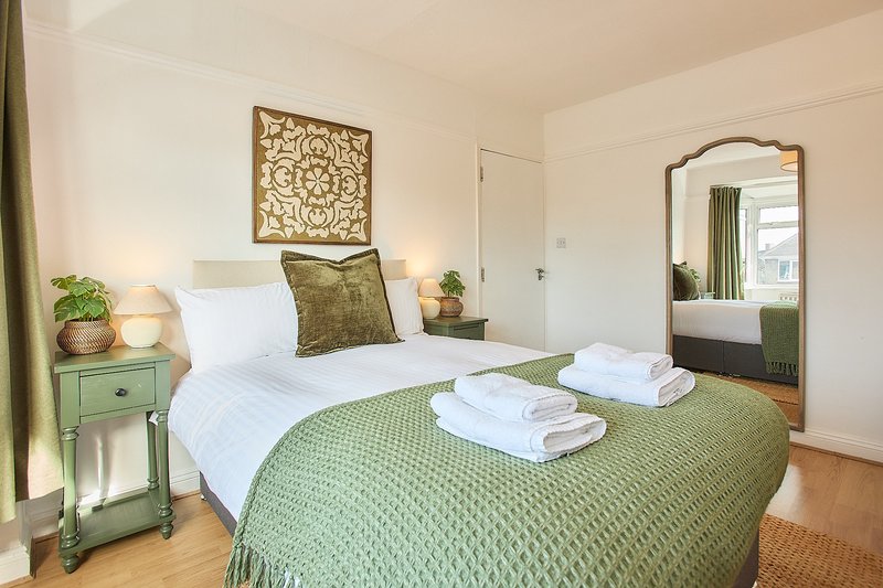 Bright bedroom with green bedside table, white bedding, green throw, and arched mirror