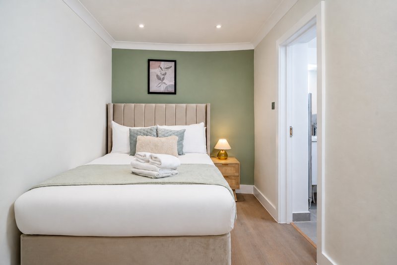 Modern bedroom with queen bed, green accent wall, bedside lamp and framed artwork