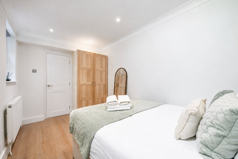 Bright bedroom with double bed, wooden wardrobe, white door and recessed lighting