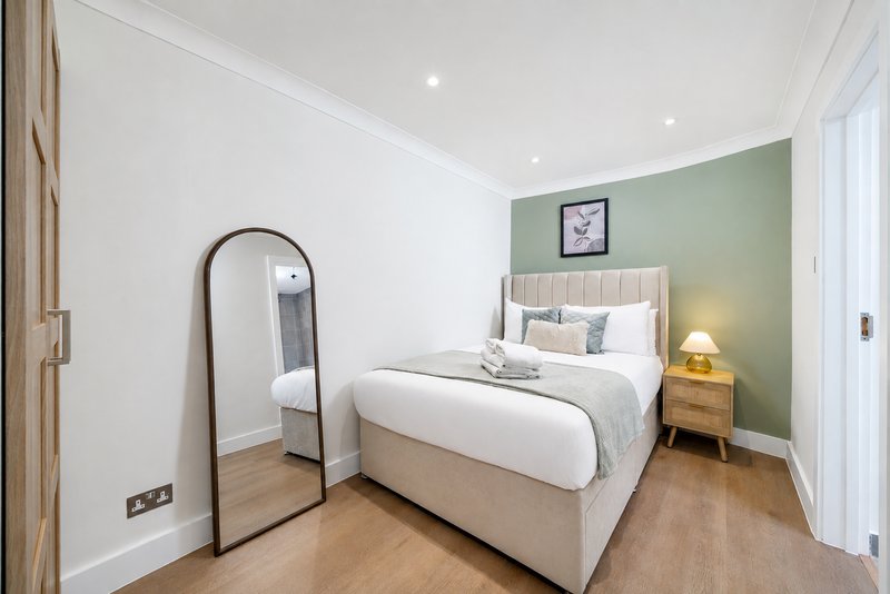 Modern bedroom with double bed, green accent wall, wooden nightstand and arched mirror