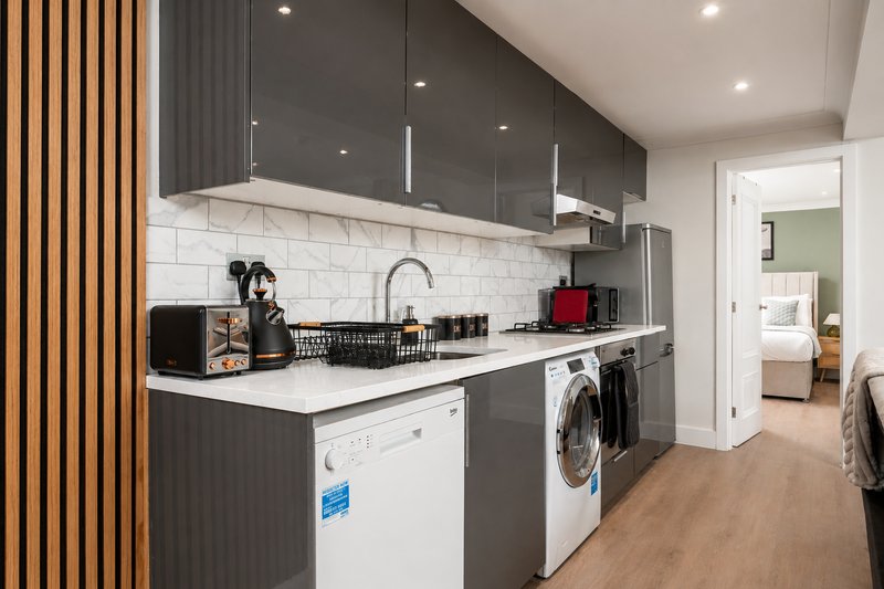 Modern kitchen with dark grey cabinetry, white countertop, integrated appliances and wooden accent wall