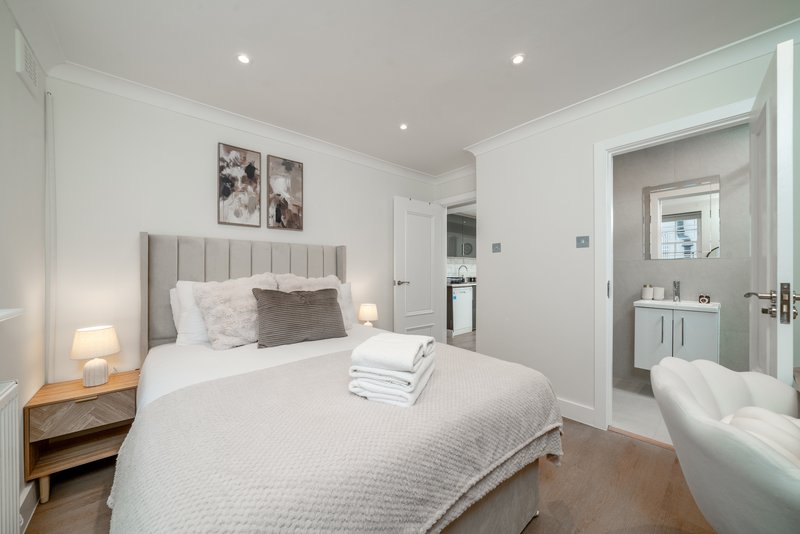 Modern bedroom with upholstered headboard, double bed, ensuite bathroom with freestanding bath visible