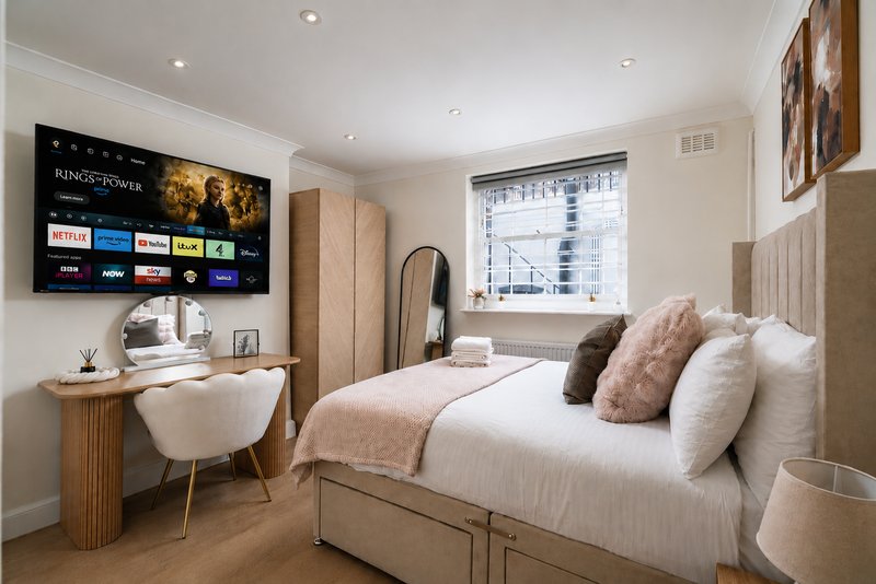 Modern bedroom with double bed, desk, wall-mounted TV, and large window with city view